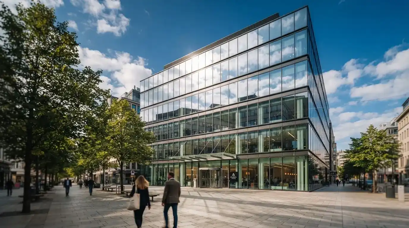 Edificio moderno de oficinas con grandes ventanales de cristal reflejando el cielo, visto desde una calle peatonal.