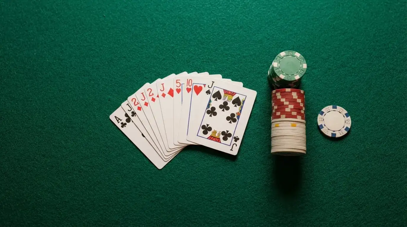 Vista cenital de una baraja de cartas y fichas de casino apiladas sobre una mesa de fieltro verde.