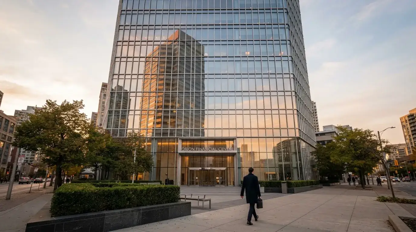 Un edificio de oficinas con fachada de cristal reflejando nubes, fotografiado desde una acera ancha por la tarde.